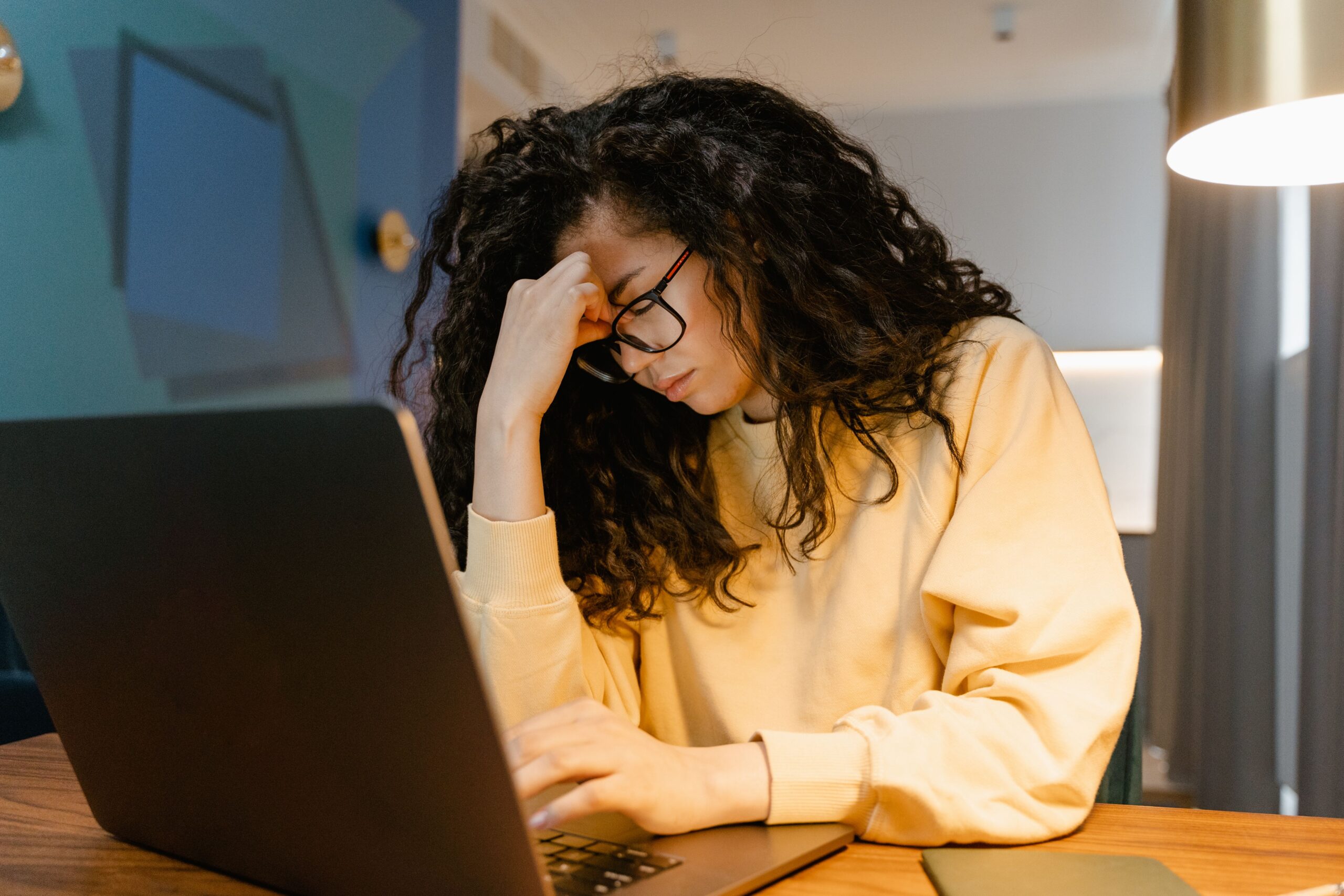woman in yellow shirt on laptop with a headache