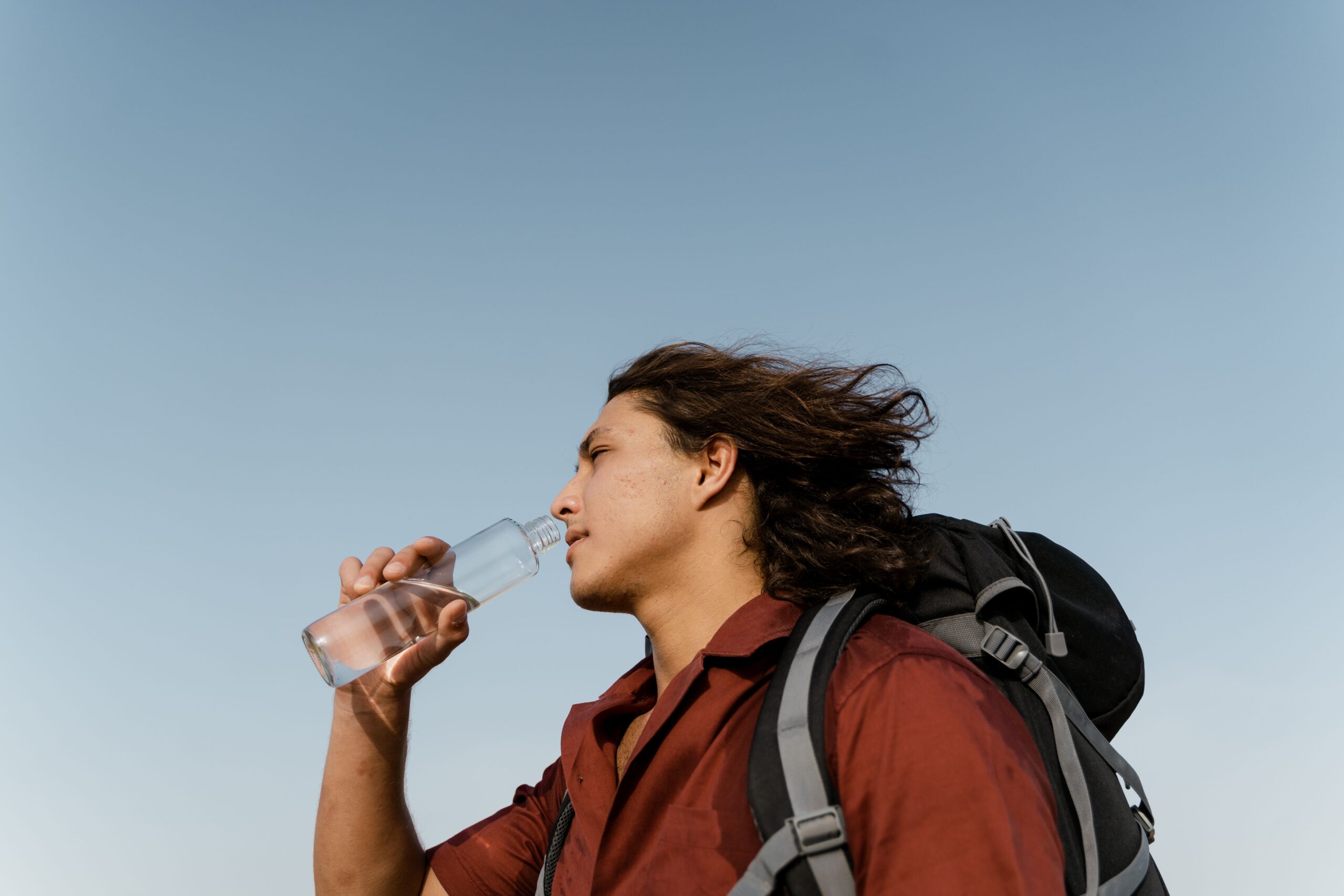 Person drinking water while wearing a backpack outdoors, illustrating how staying hydrated may help reduce dehydration-related headaches.