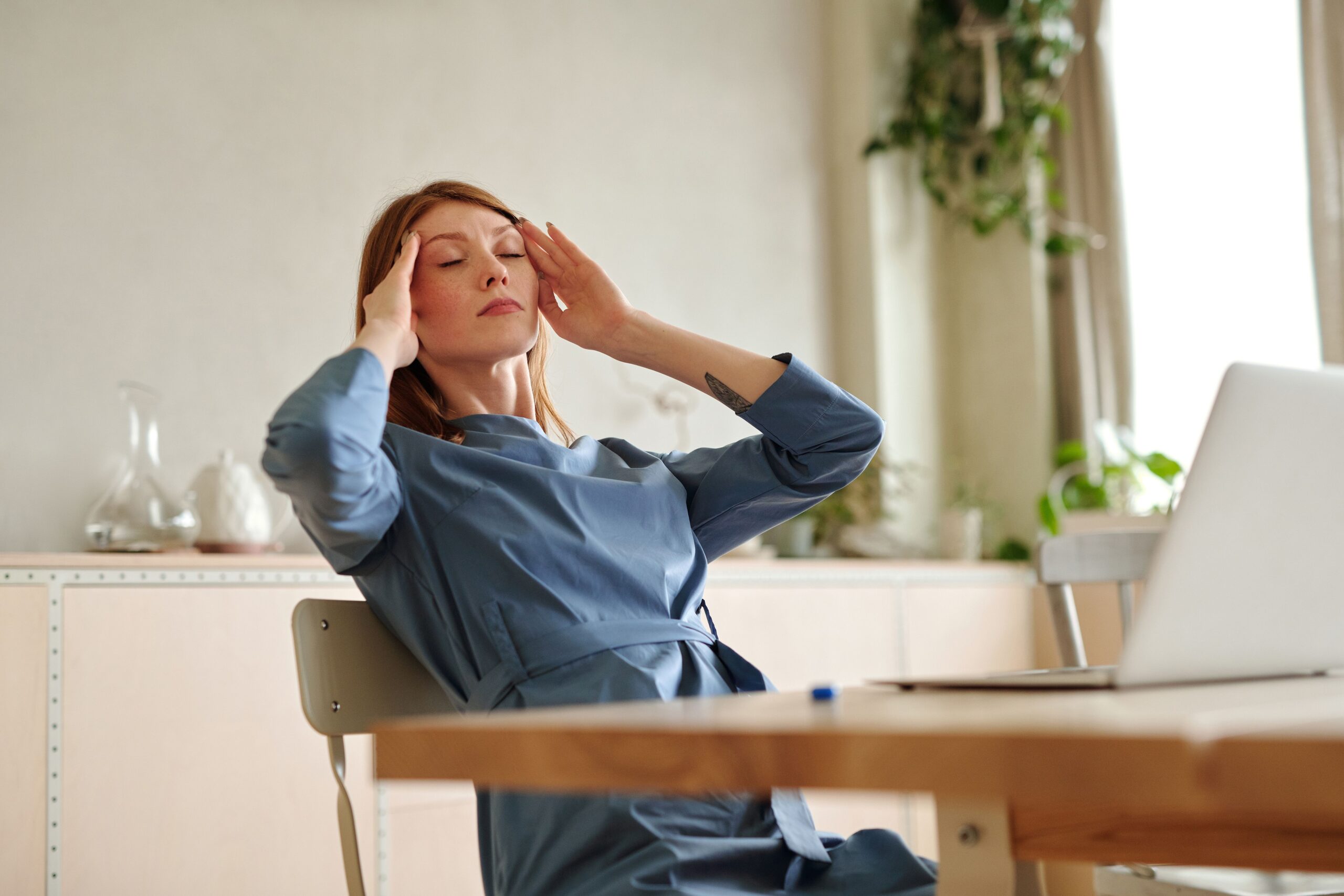 Woman experiencing a headache while working at a desk, illustrating how poor posture and prolonged computer use can contribute to recurring headaches.