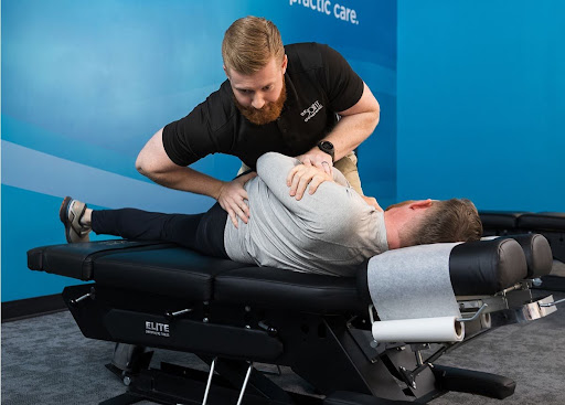  A licensed chiropractor in a black polo shirt performs a manual low back pain adjustment on a patient lying on a specialized chiropractic table.