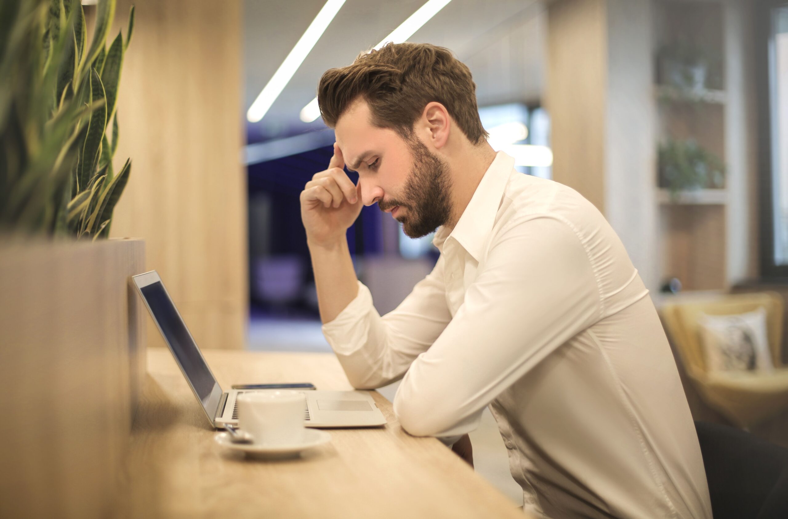 Man experiencing a headache while working on a laptop at a desk