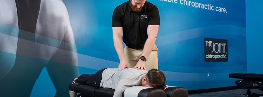 A male patient receives a spinal adjustment from a The Joint chiropractor to the upper back.